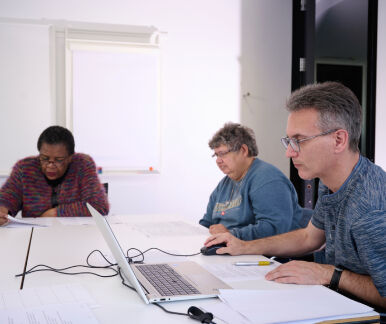 Drei Personen sitzen an einem Tisch und lesen konzentriert Texte Drei Personen sitzen an einem Tisch und lesen konzentriert Texte